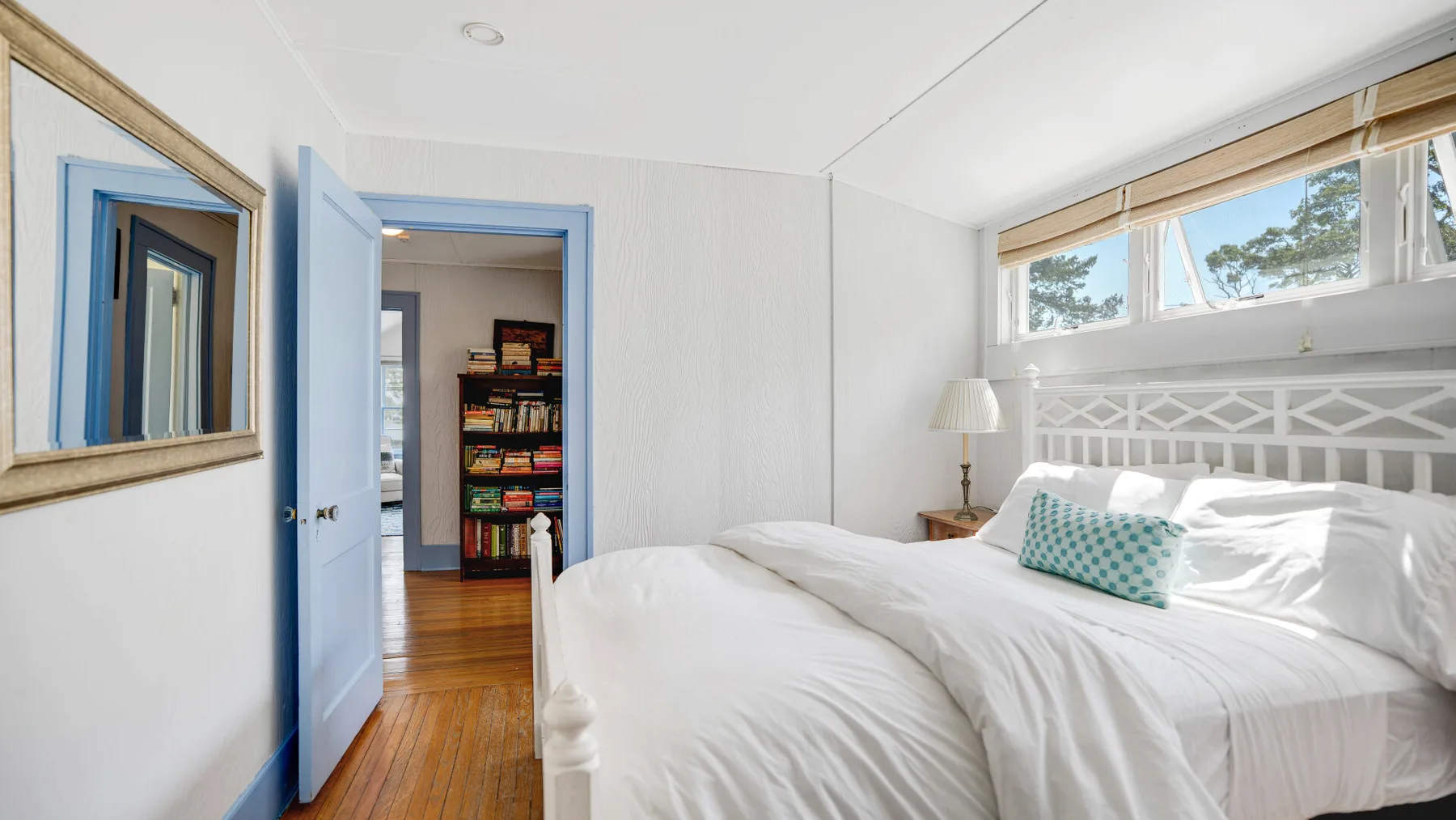 A bright bedroom with white bedding and a window above the bed.