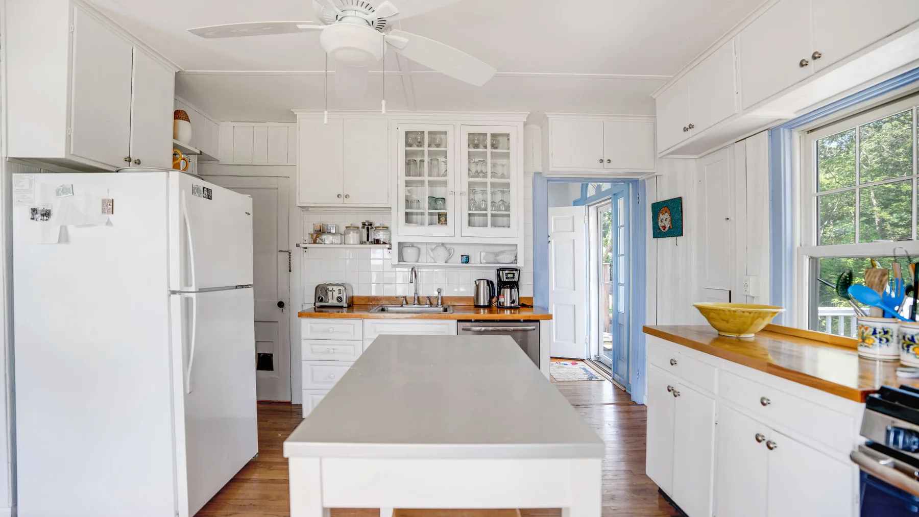 A bright kitchen with white cabinets, a central island, and large windows.