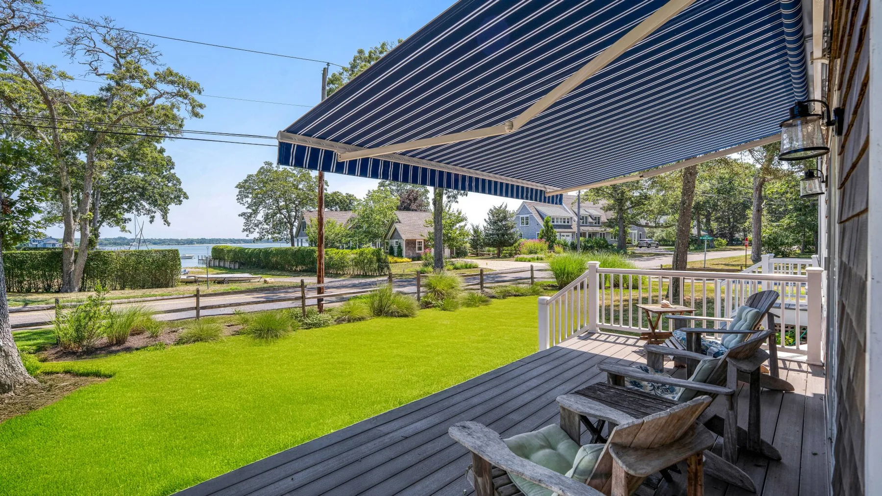 A shaded outdoor deck with seating overlooks a green lawn and nearby water.