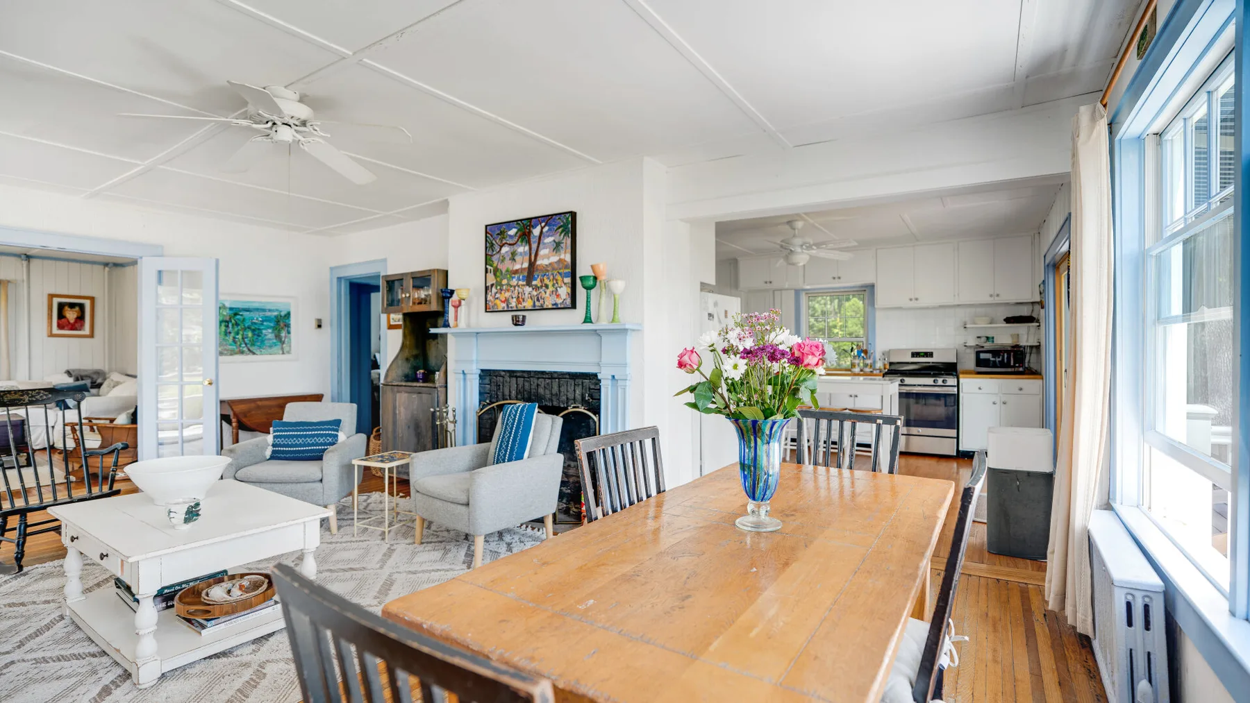 A bright living and dining area opens onto a kitchen, with a wooden dining table.