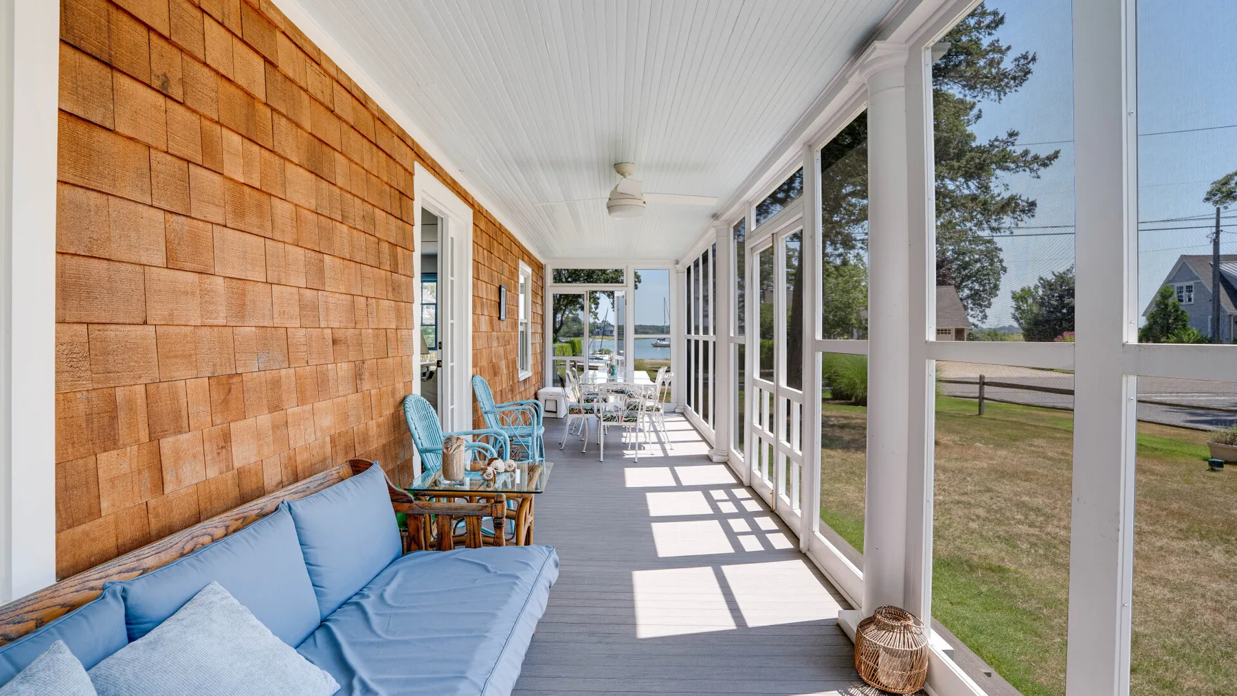 A bright screened porch with blue seating and large windows overlooking the yard.