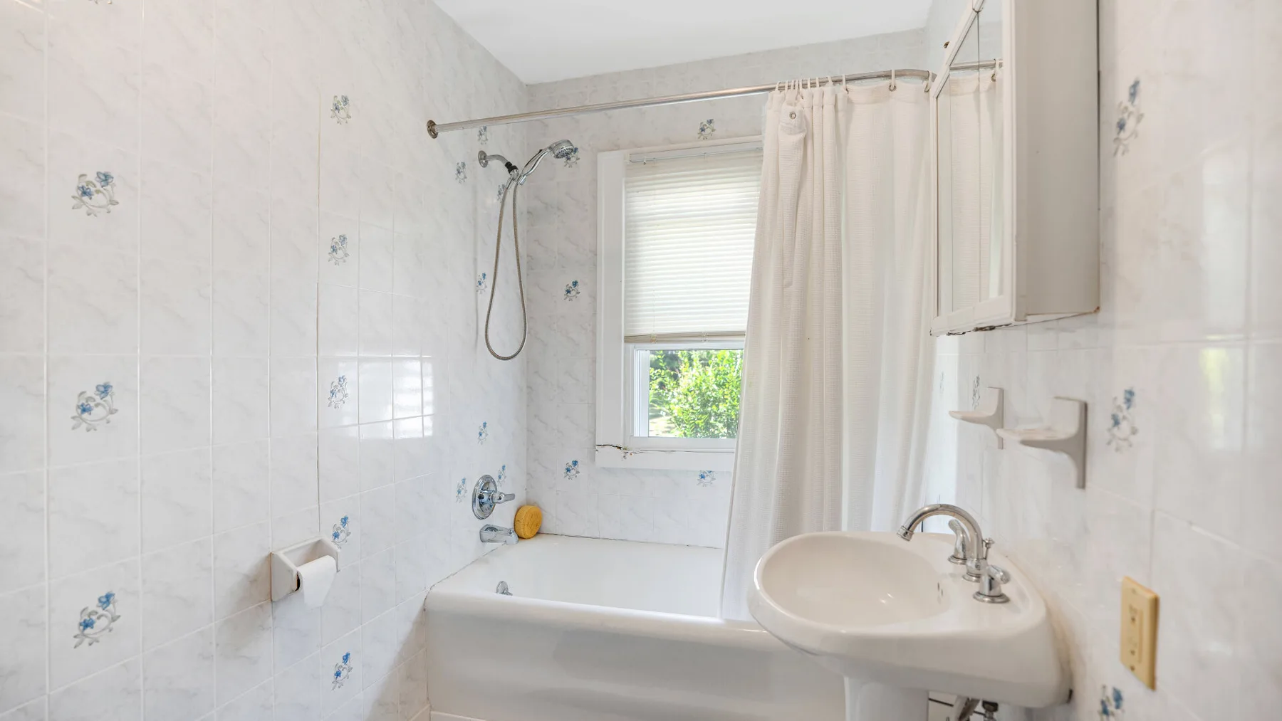 A tiled bathroom with a bathtub, shower, and sink beside a window.