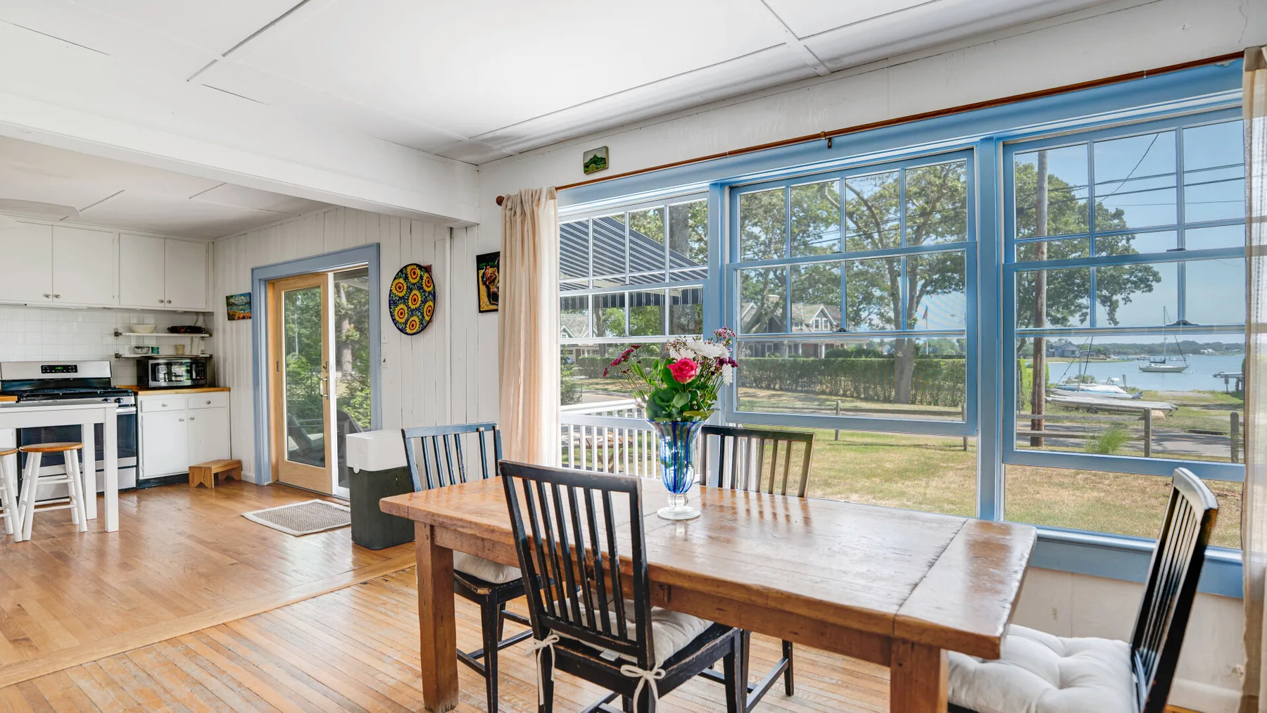Dining area with a wooden table beside large windows overlooking the water.