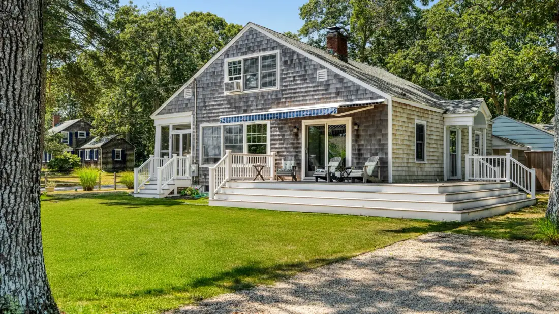 A gray shingle-sided house with a broad deck and green lawn.