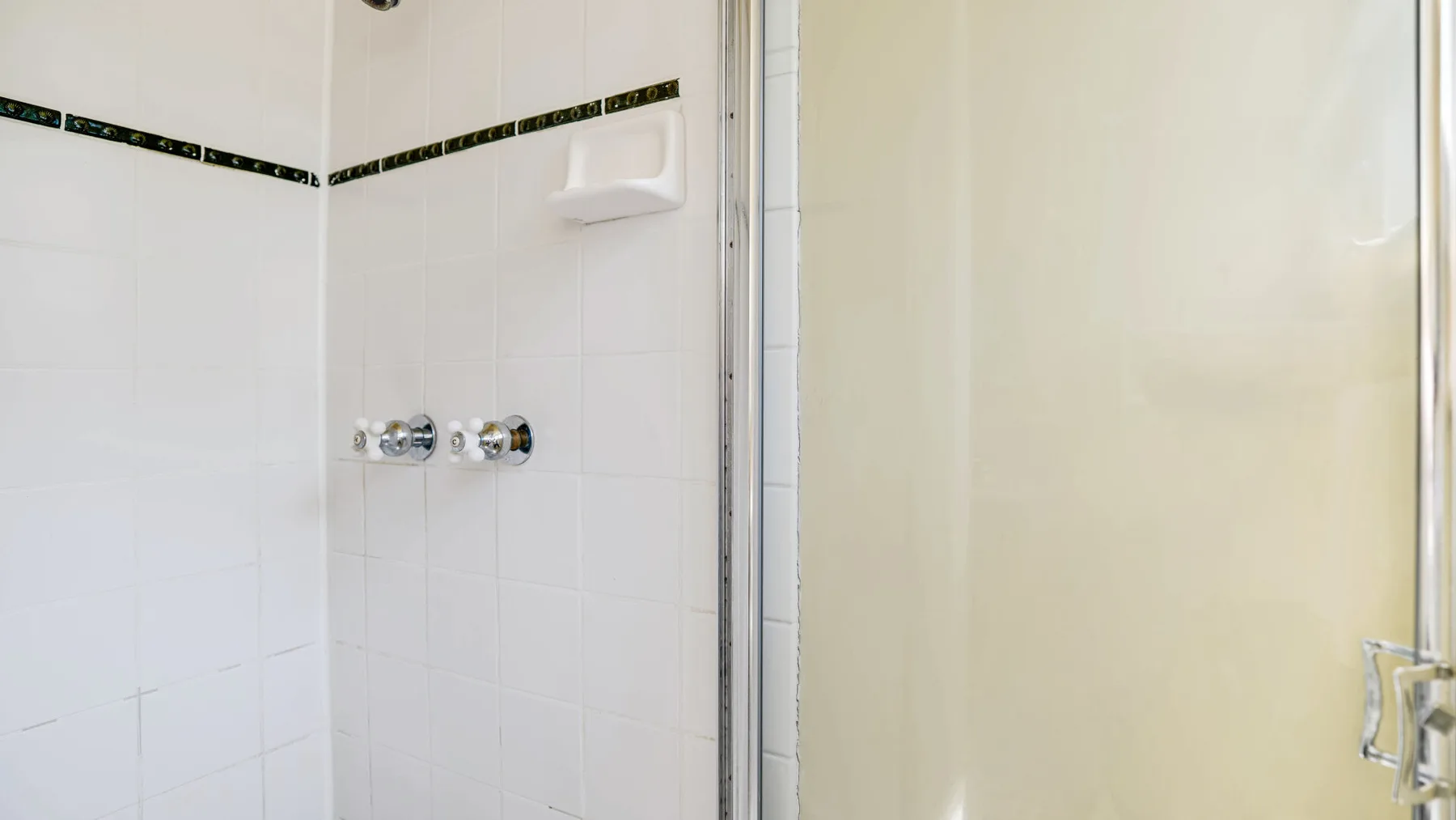 A tiled shower area with wall-mounted controls and a soap dish.