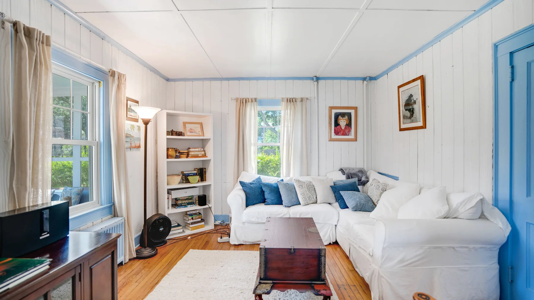 A bright living room with white seating, blue cushions, and a coffee table.