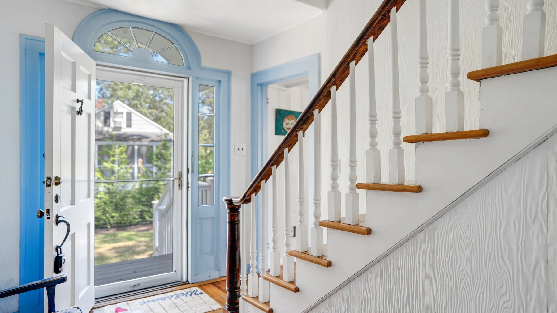 A bright entry hall with a glass front door and staircase.