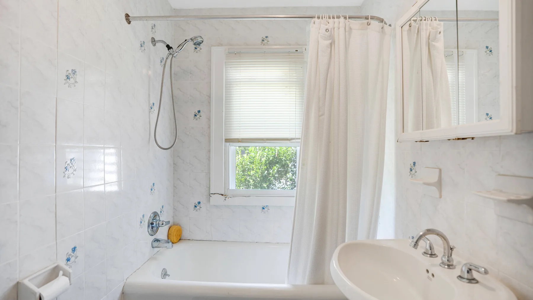 A bright bathroom with a bathtub, shower, window, and sink.