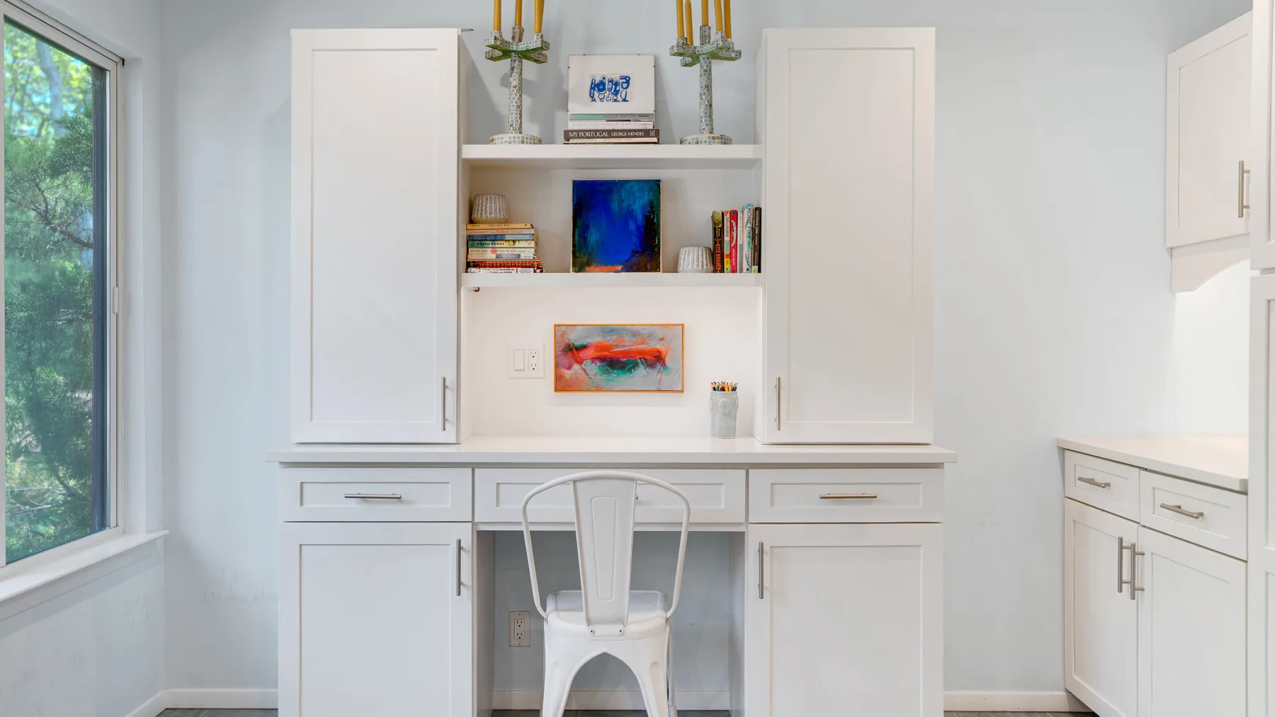 Una cocina blanca y luminosa con armarios empotrados y una pequeña zona de escritorio.
