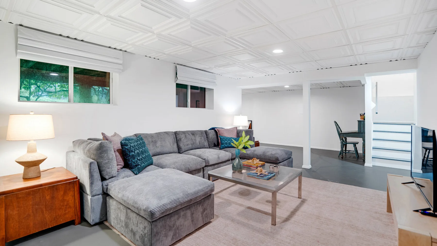 Una sala en el sótano con asientos seccionales, una mesa de centro y ventanas pequeñas.