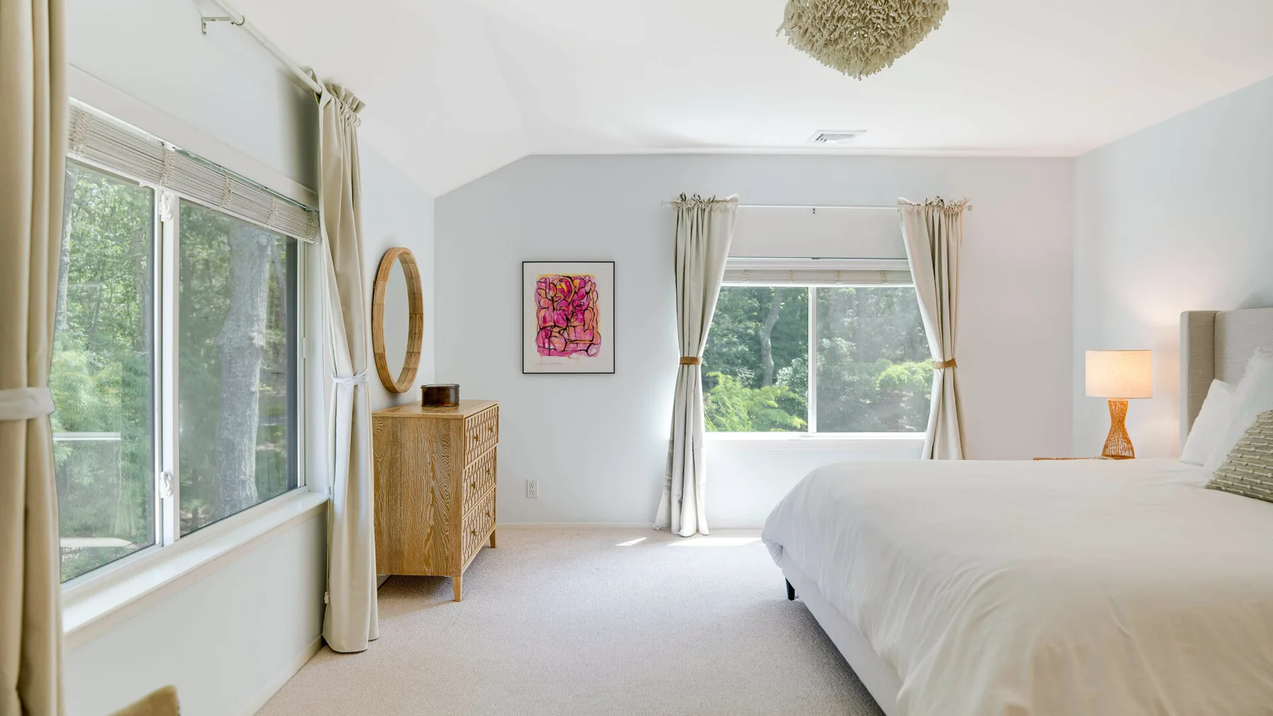 Un dormitorio luminoso con una cama grande y ventanas con vistas a la vegetación.