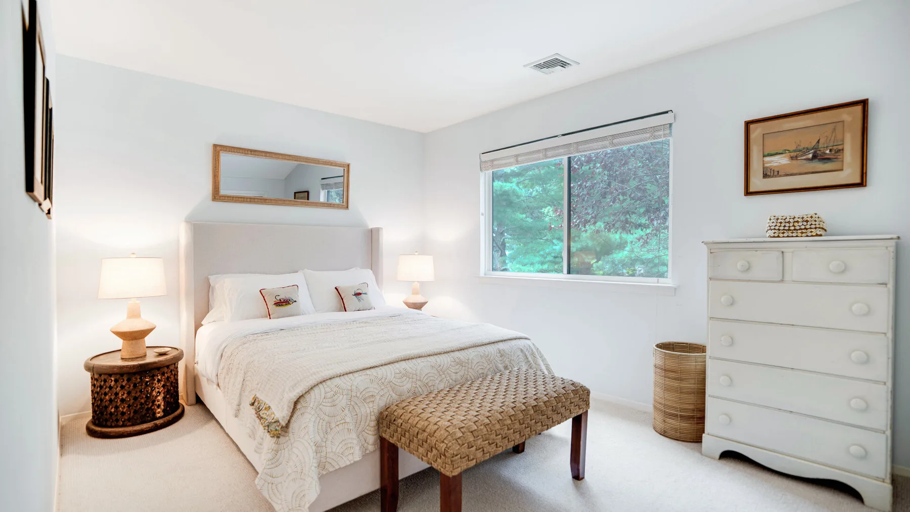 Un dormitorio luminoso con una cama blanca, mesitas de noche y una ventana grande.