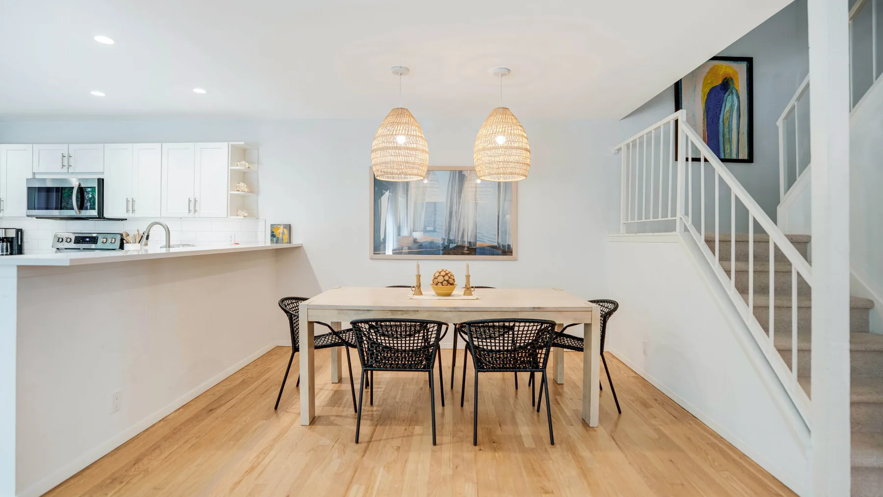 Un comedor luminoso con mesa y sillas junto a una cocina abierta y una escalera.