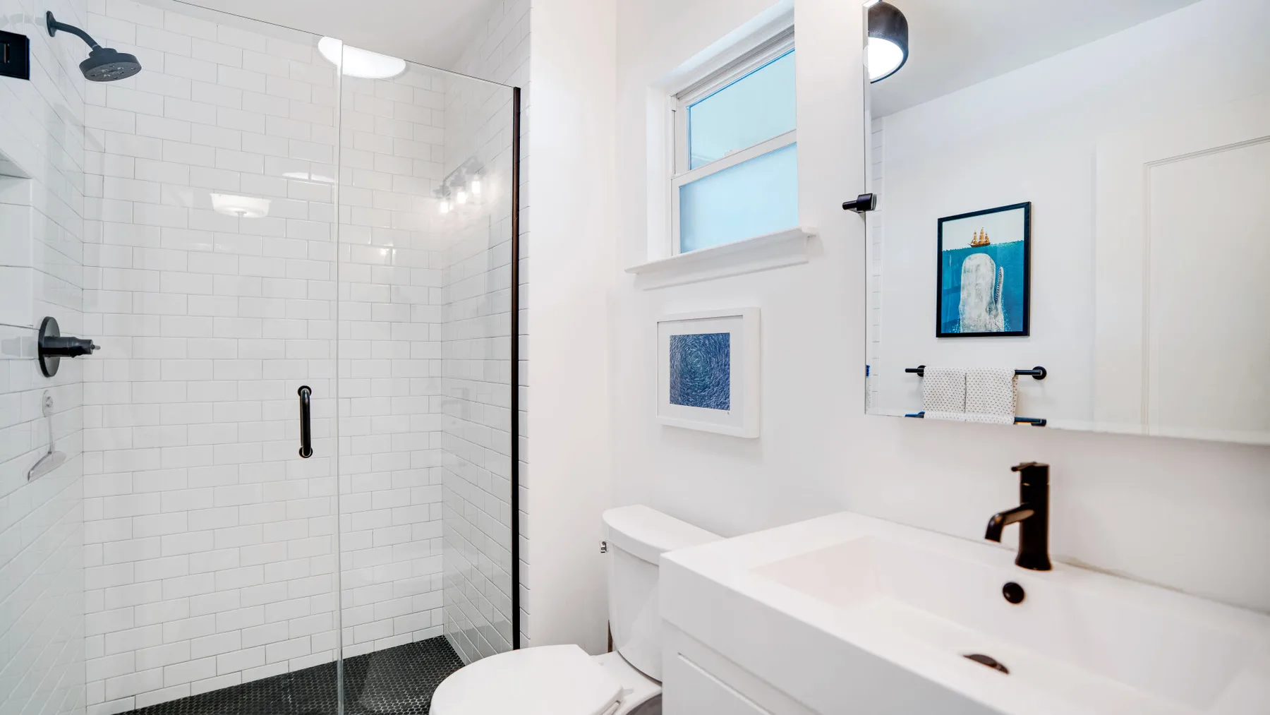 Un baño luminoso con una ducha de azulejos y un lavabo bajo un espejo.