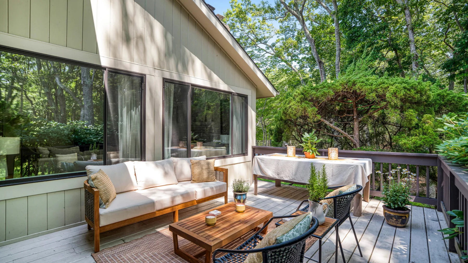 Una terraza exterior tiene asientos acolchados junto a una mesa con plantas en macetas.
