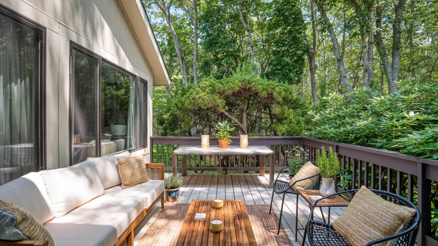 An outdoor deck with seating and a wooden table, surrounded by greenery.