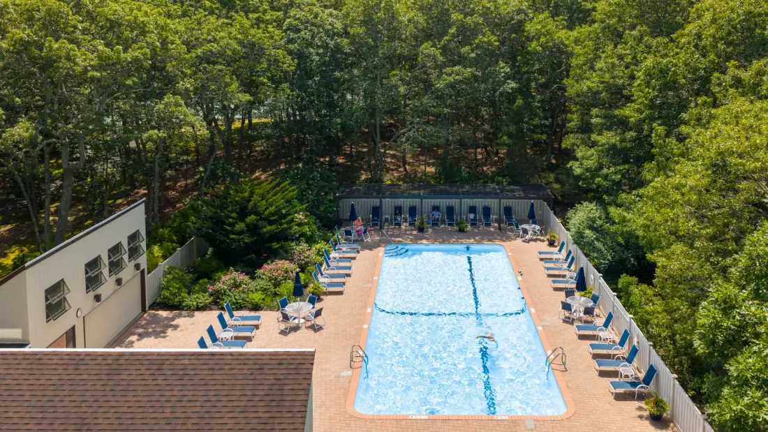 Una piscina al aire libre está rodeada de asientos reclinables y árboles.