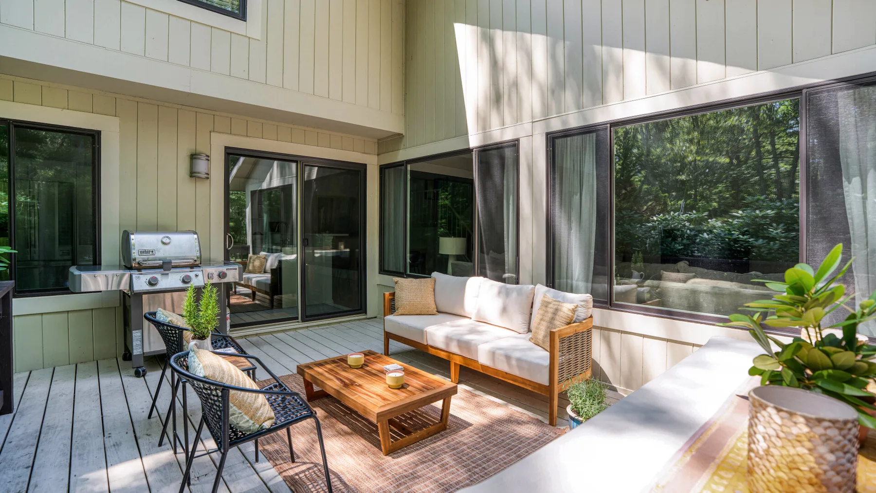 A sunlit outdoor seating area with a table and large windows overlooking greenery.