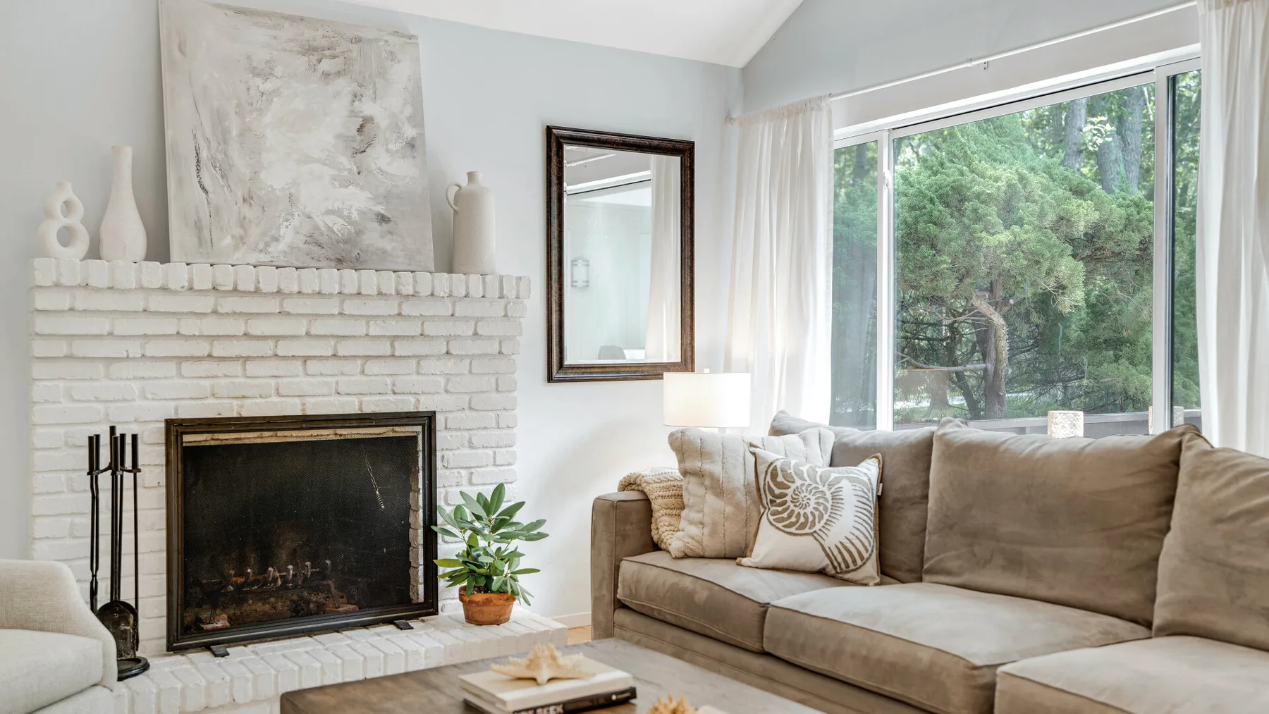 Una sala luminosa con chimenea, asientos y una gran ventana con árboles a la vista.