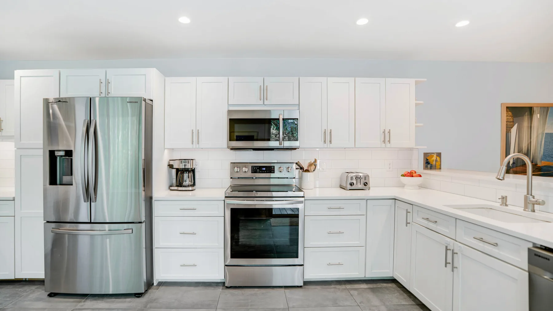 Una cocina blanca y luminosa con electrodomésticos de acero inoxidable y una encimera larga.