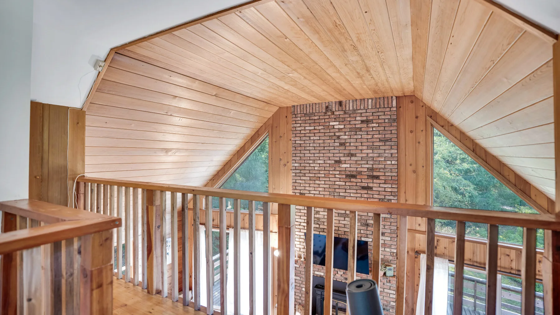 A wood-paneled loft overlooks a brick fireplace and windows.