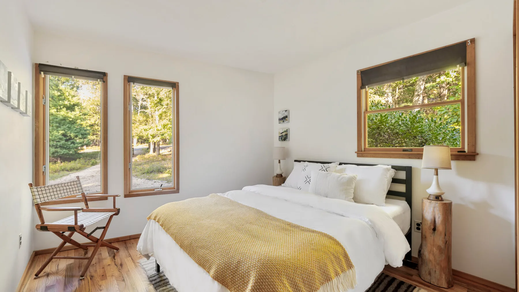 A bright bedroom with a neatly made bed and large wood-framed windows.