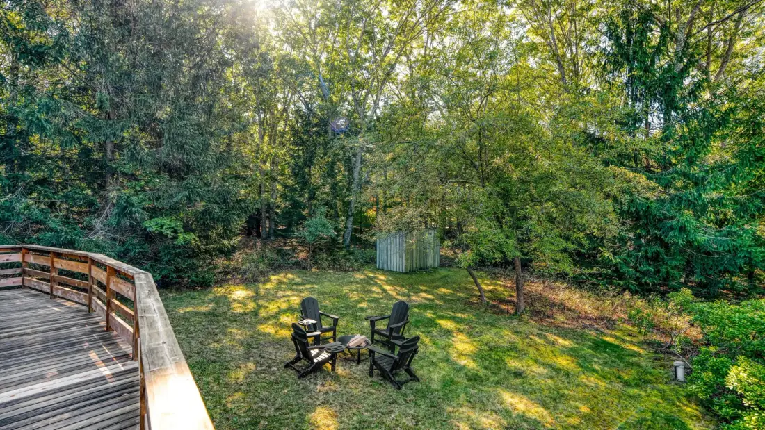 A wooden deck borders a leafy yard with two chairs.