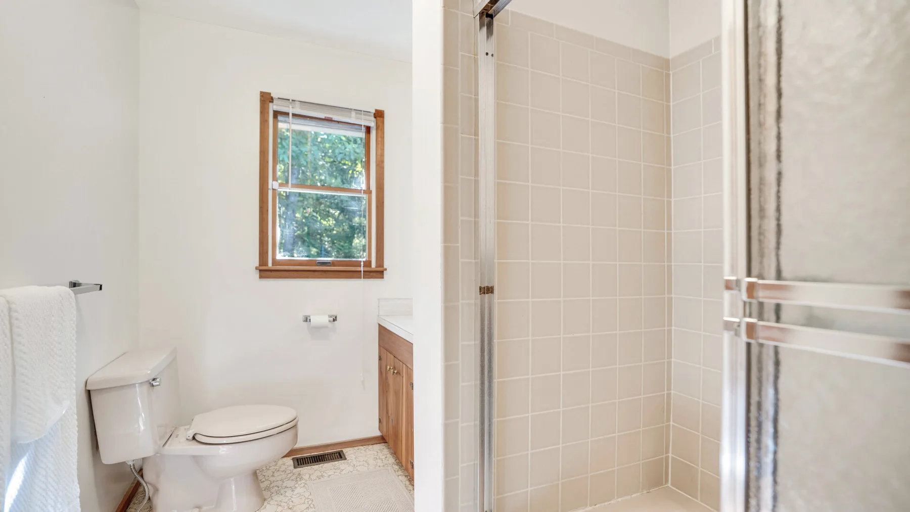 A bright bathroom with a tiled shower, toilet, and window.