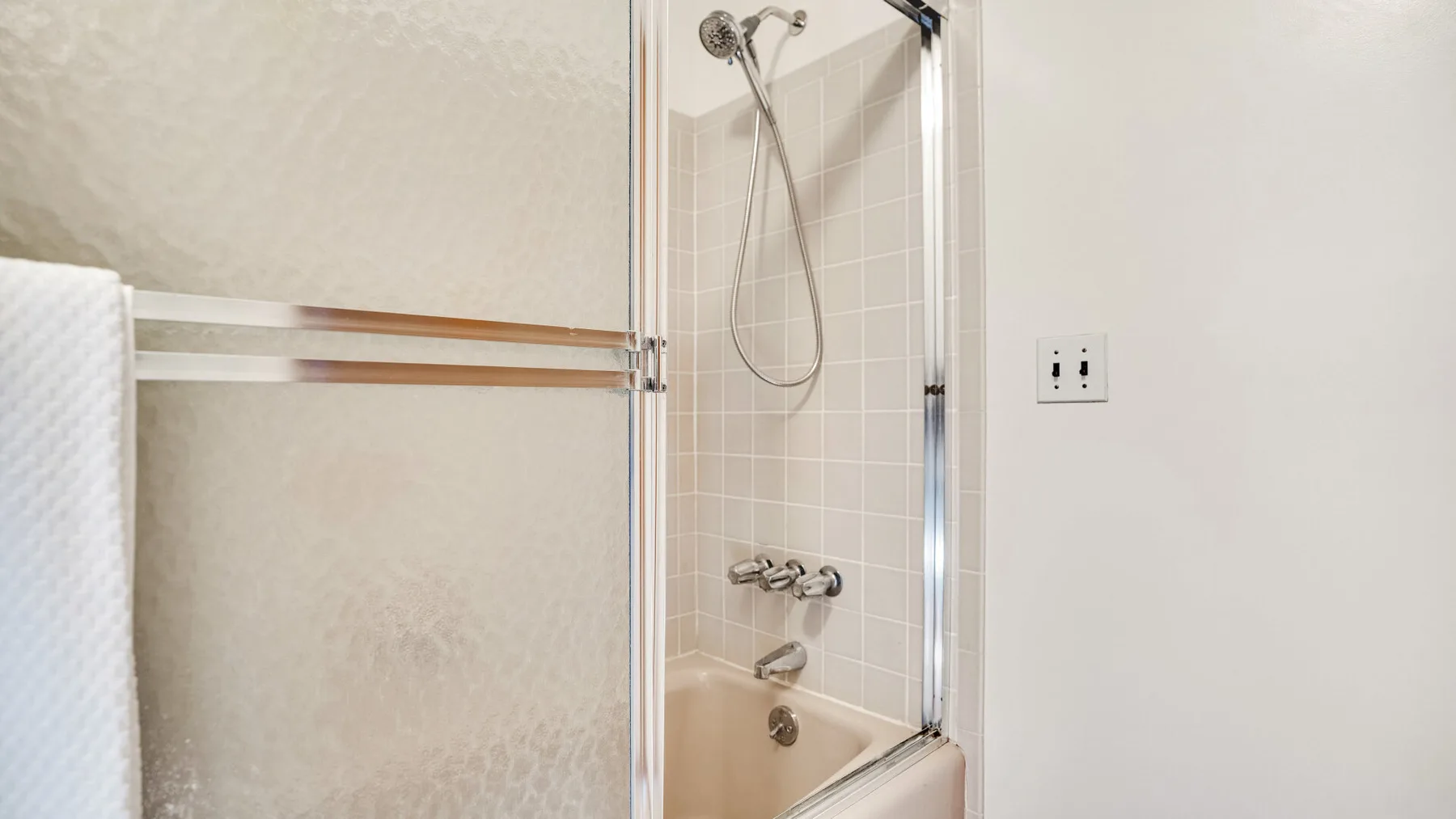 A bathroom shower with tiled walls and a towel hanging nearby.