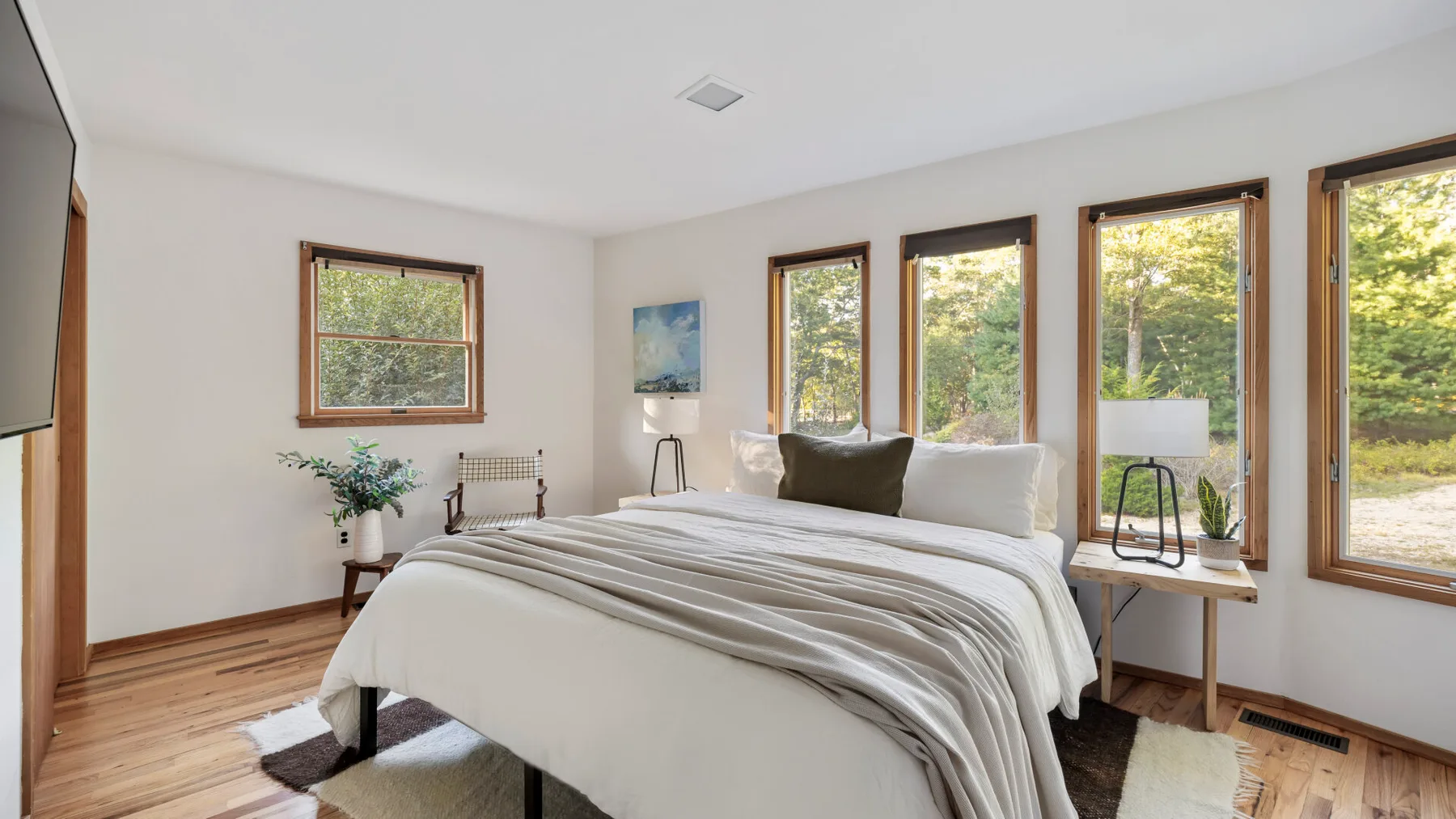 A bright bedroom with a neatly made bed beside several tall windows.