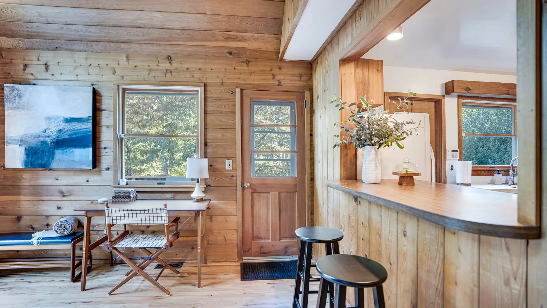 A wood-paneled room with a small table, seating, windows, and a counter.