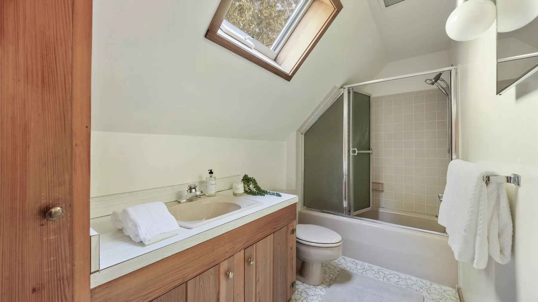 A bathroom with a sink, toilet, and bathtub beneath a sloped ceiling.