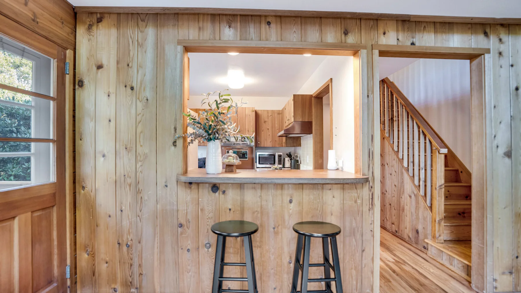 A wood-paneled room opens onto a kitchen counter and staircase.