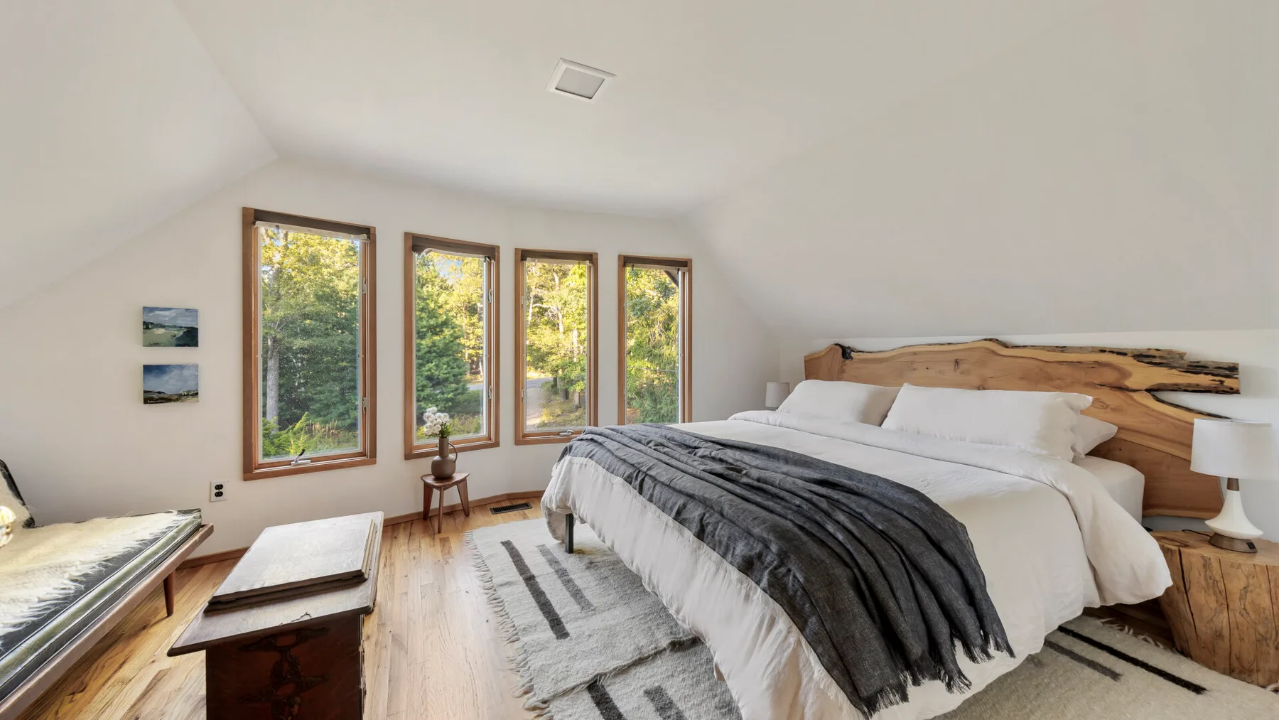 A bright bedroom with a large bed and windows overlooking trees.