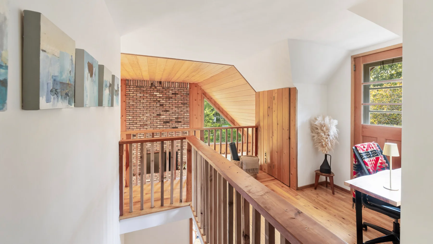 A bright interior landing with a wooden railing, wall art, and a window.