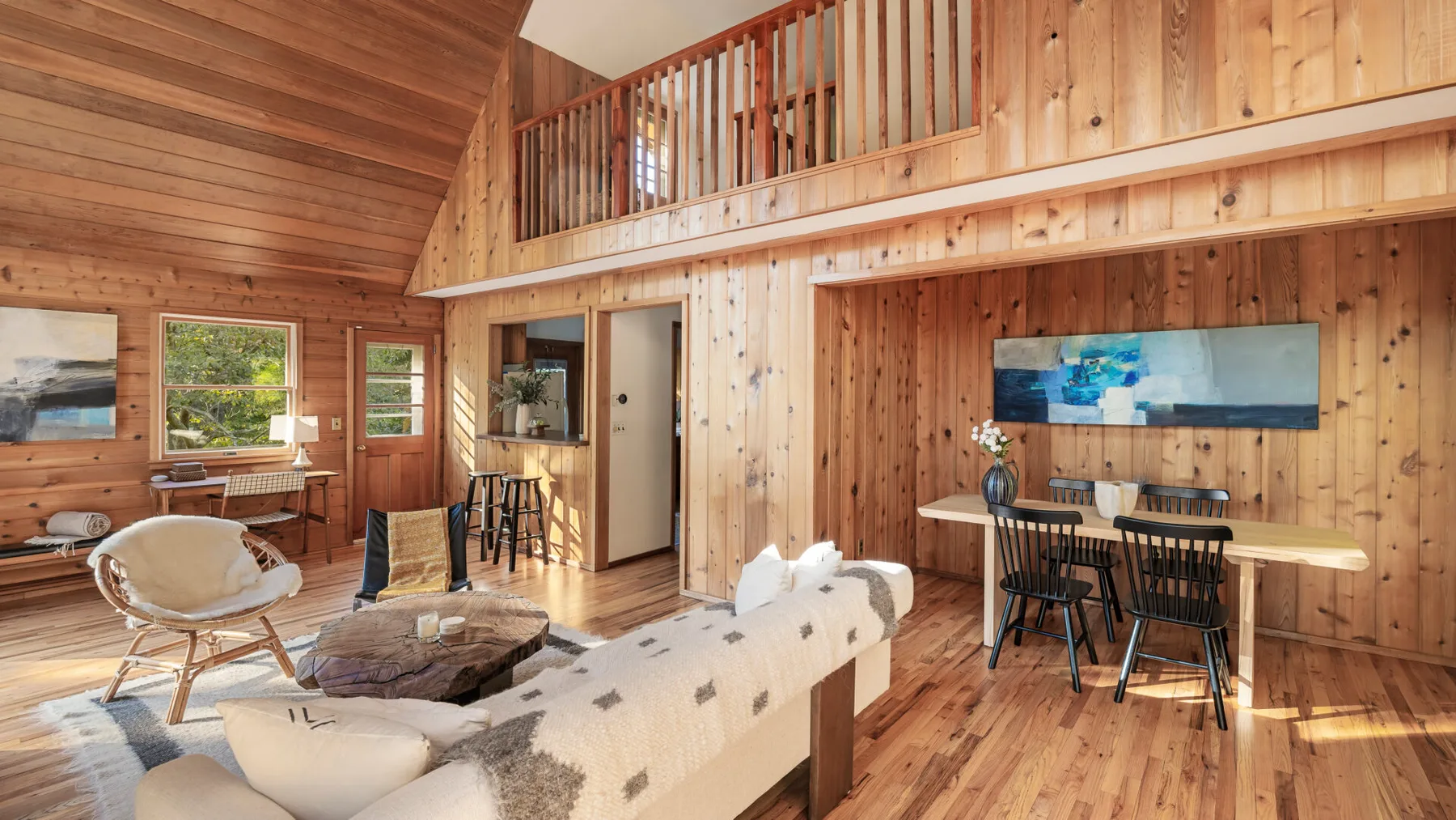 A wood-paneled living room with seating, a dining table, and an upper-level railing.