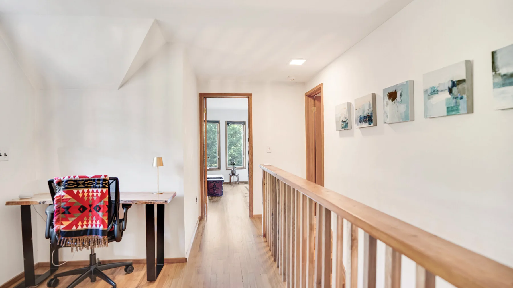 A bright hallway with a wooden railing and framed artwork along the wall.