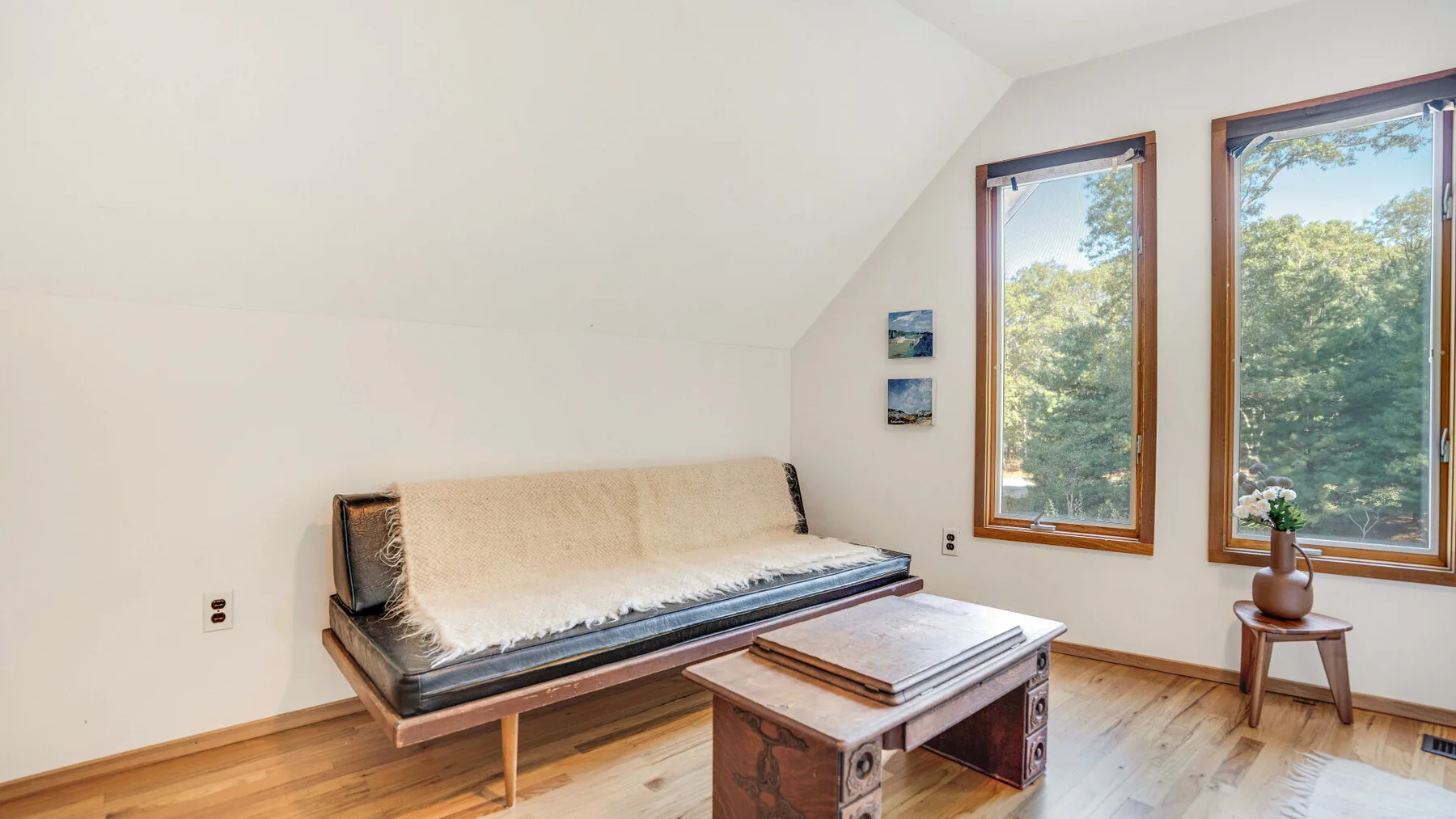 A bright sitting area with a daybed, wooden coffee table, and tall windows.