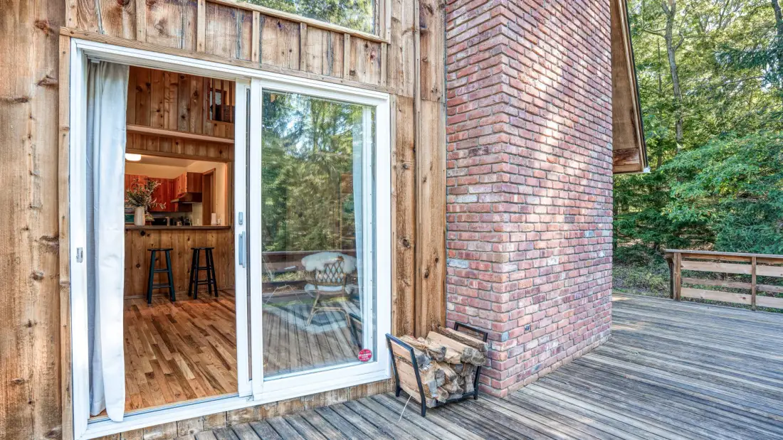 A wooden deck beside a brick wall, with sliding glass doors opening onto an interior.