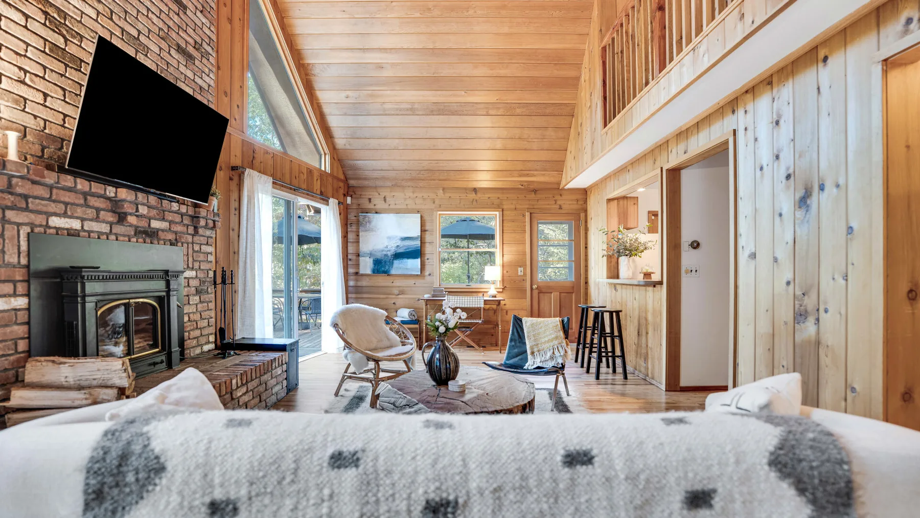 A bright wood-paneled living room has a brick fireplace and seating by large windows.