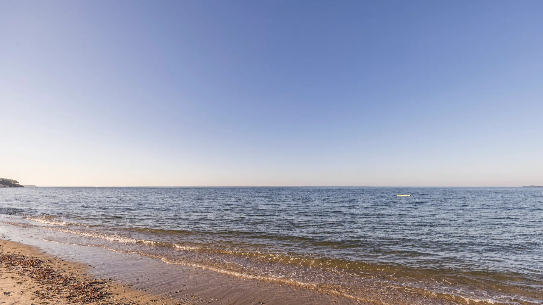 A sandy beach meets calm water beneath a clear sky.