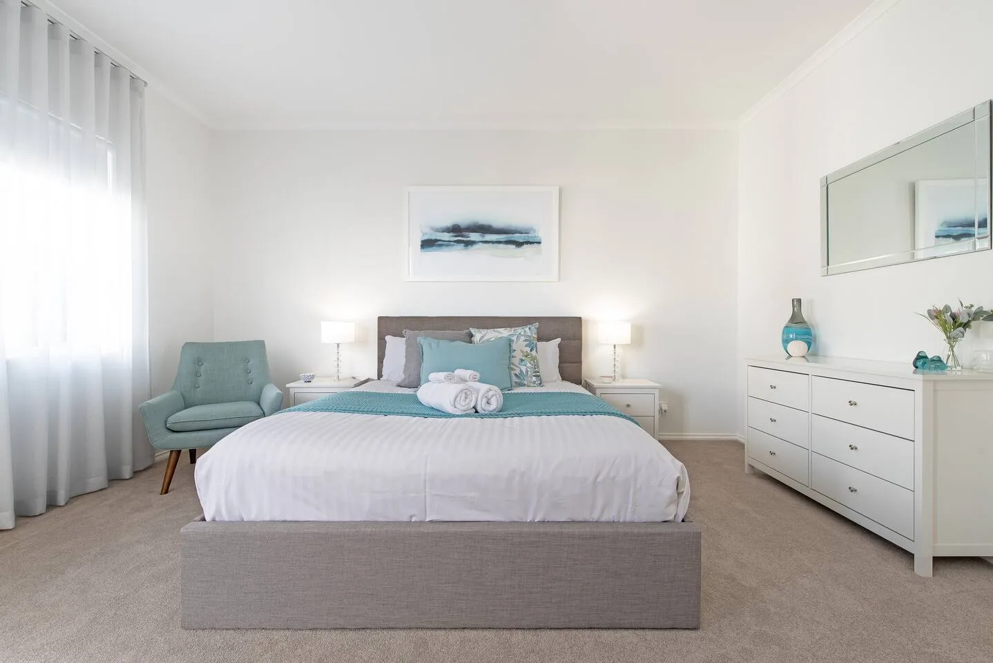 Un dormitorio luminoso con una cama bien hecha y una cómoda junto a la pared.