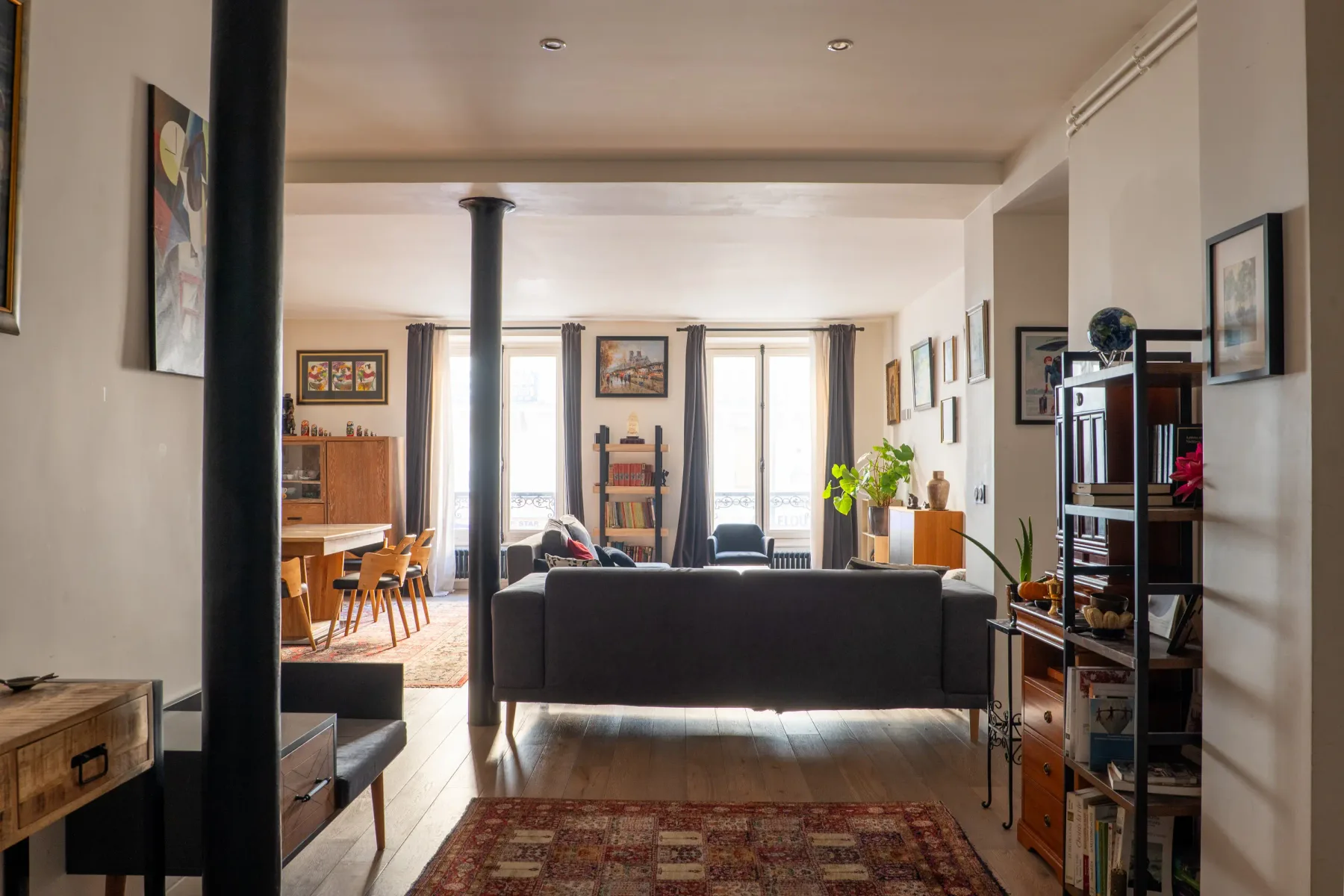 Living room with a dark sofa facing tall windows and a dining area beyond.