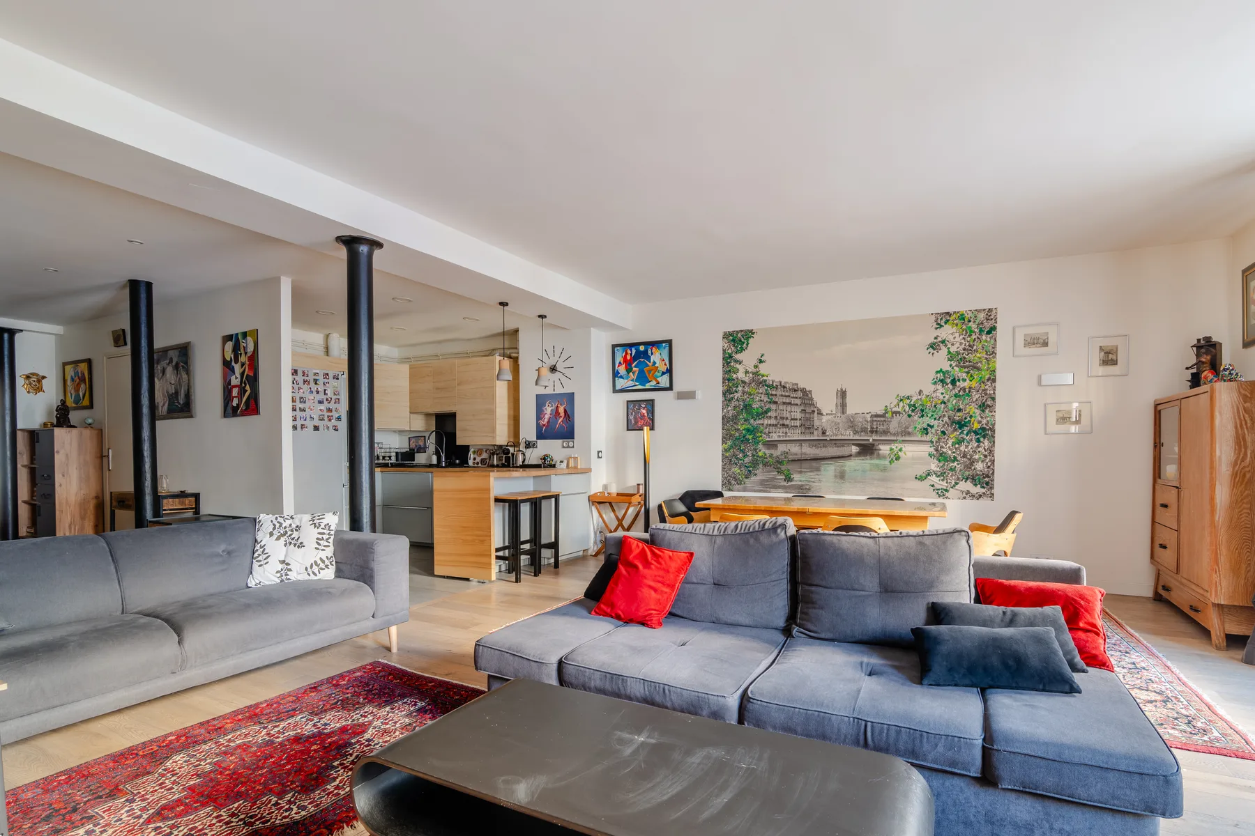 An open-plan living room has gray seating, a coffee table, and a kitchen area.