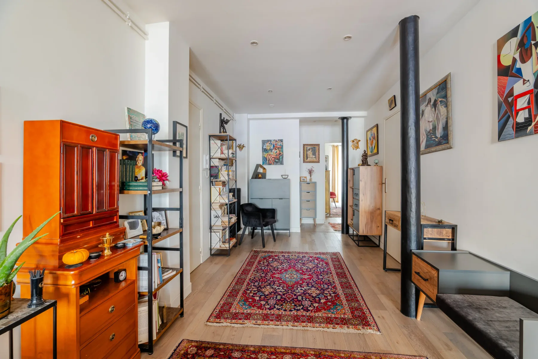 A long living room with a patterned rug and colorful wooden cabinet.