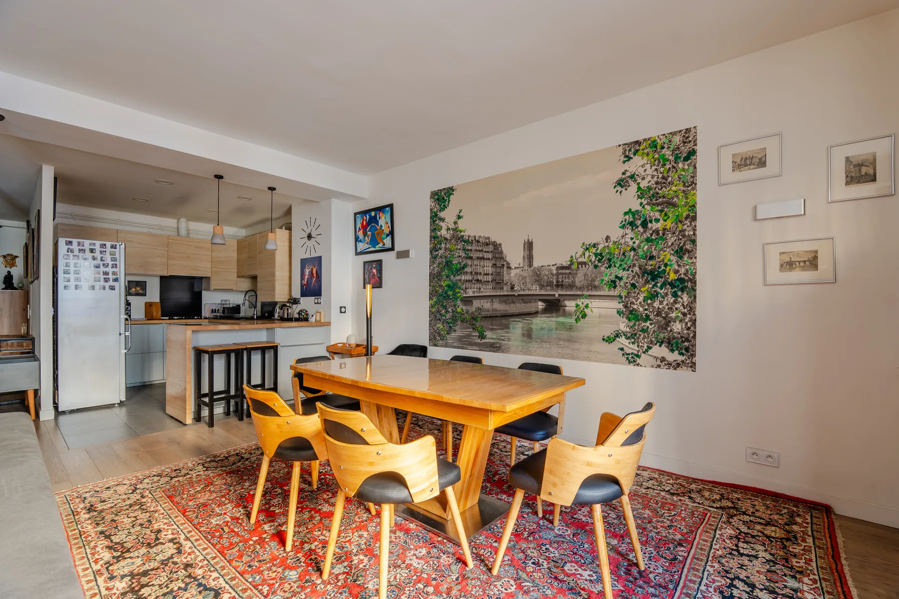 A dining area with a wooden table and colorful rug beside an open kitchen.