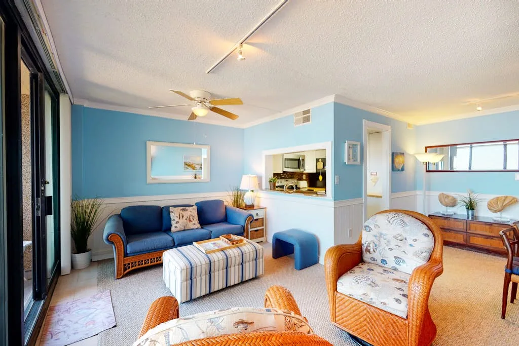 A bright living room with blue seating and a striped ottoman.