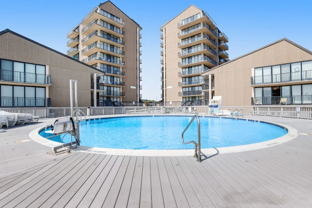 An outdoor swimming pool is surrounded by a broad deck and apartment buildings.