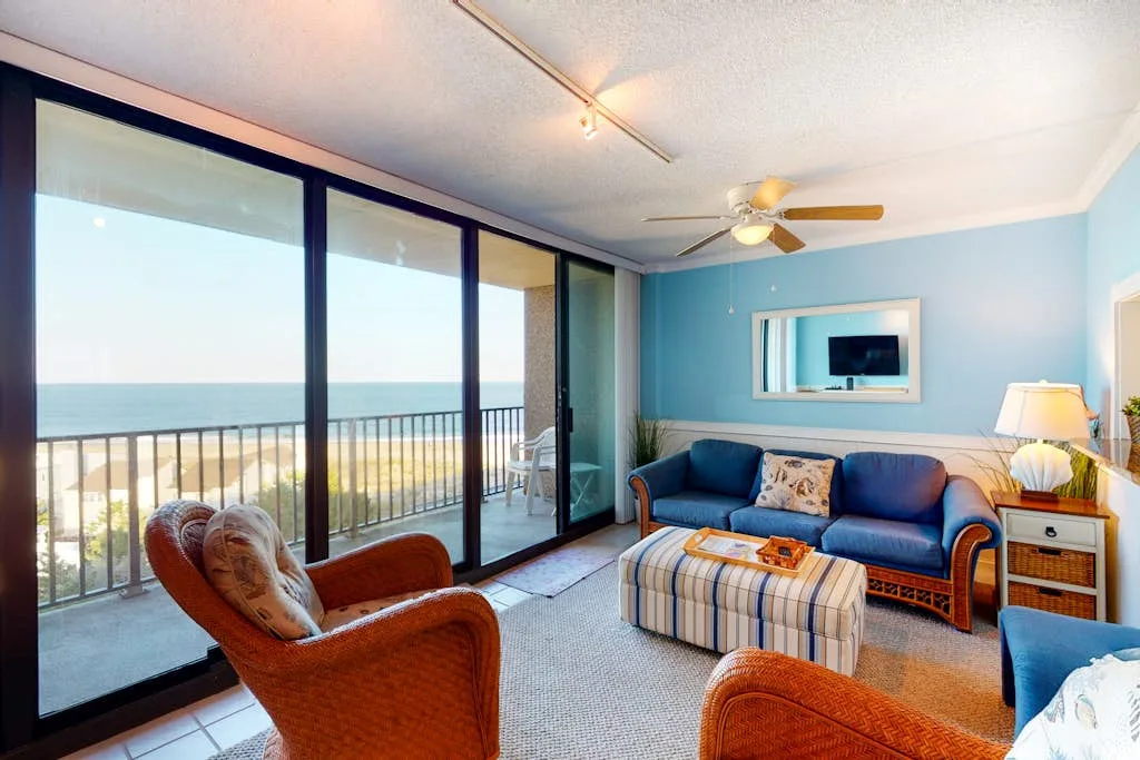 A living room with blue seating and large windows overlooking the ocean.