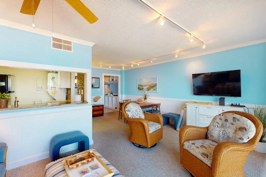 A bright living room with wicker seating and a wall-mounted television.
